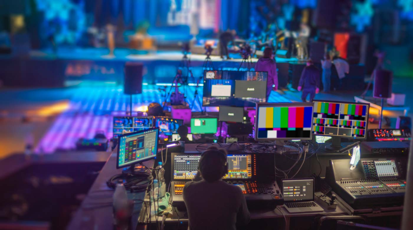 Virtual event mixing board, video monitors and engineer facing a concert stage